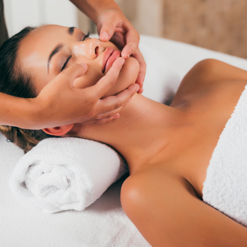 A therapist's hands working a client's face and jawline during a head massage session.