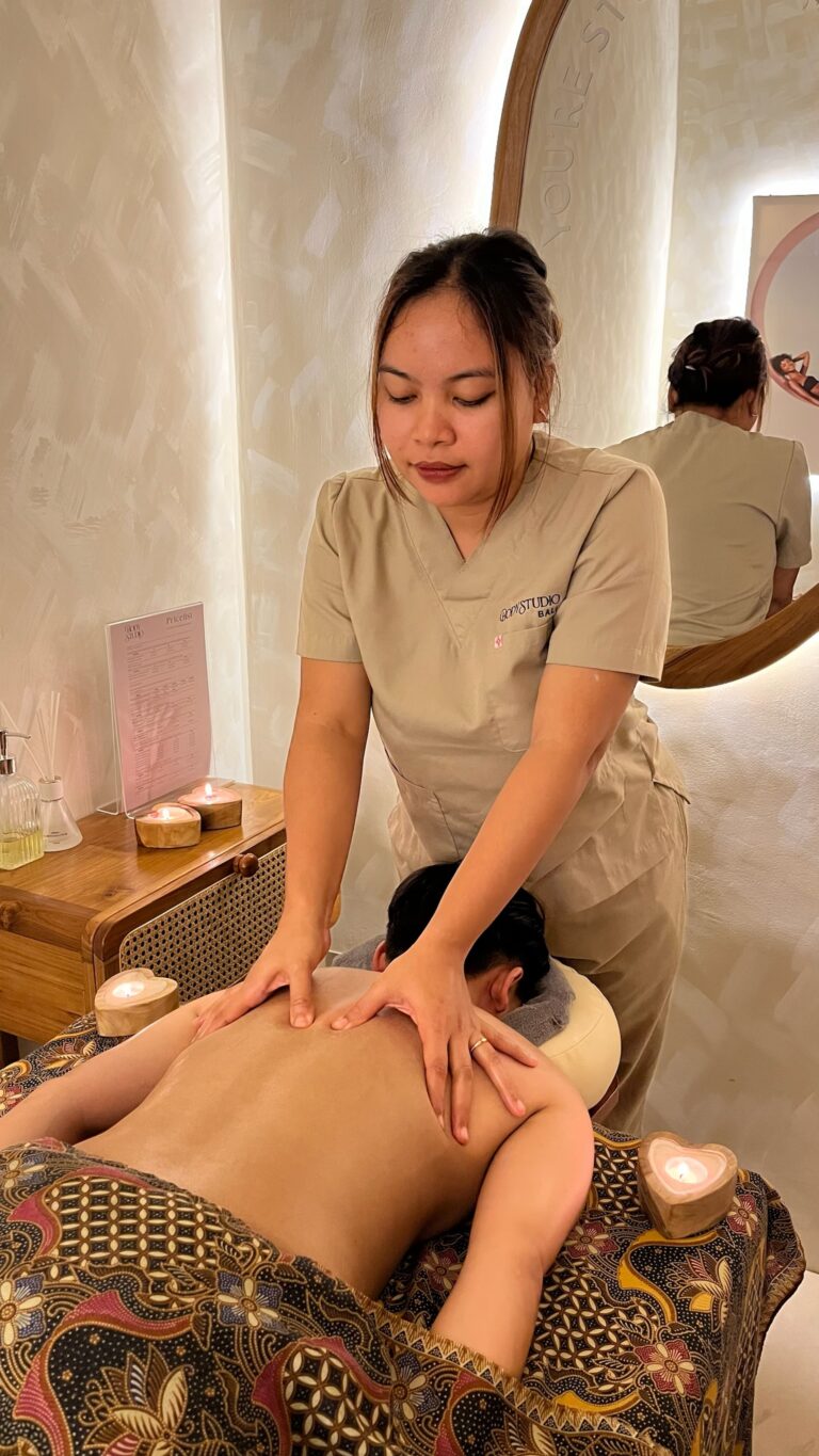 A therapist performs a hands-on back massage on a client lying face down in a treatment room.