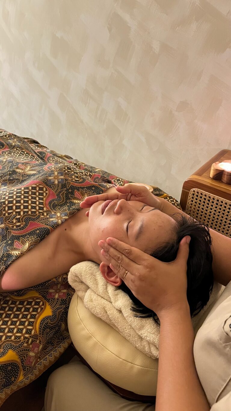A therapist massages a client's face as she lies on a treatment bed.