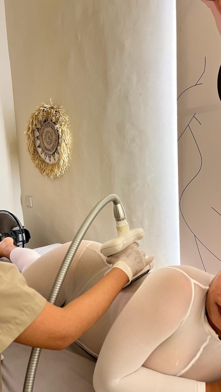 A therapist uses an LPG endermologie roller handpiece on a client's hip over a white treatment suit.