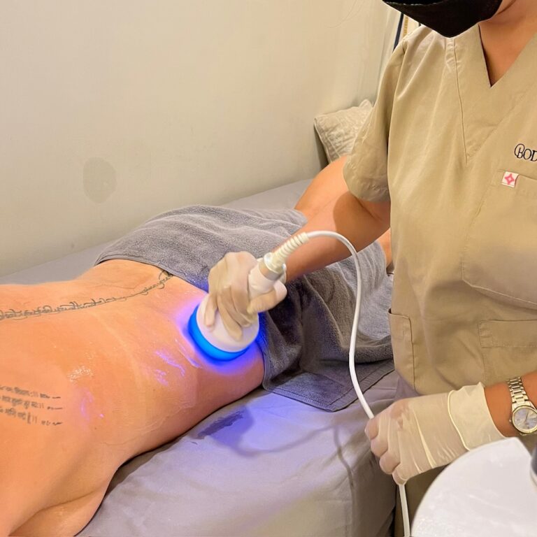 A therapist applies a handheld cavitation probe to a client’s upper thigh.