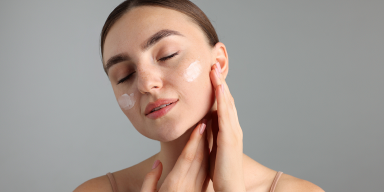 A woman applies skincare cream to her cheeks.