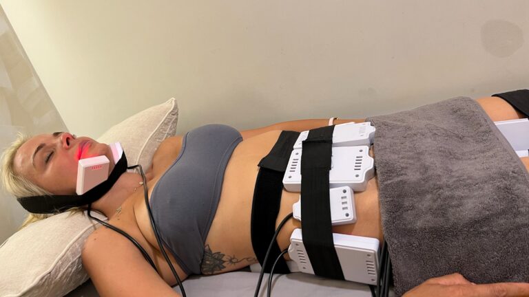A client receives cold lipo laser treatment with pads secured to the abdomen and under the chin.