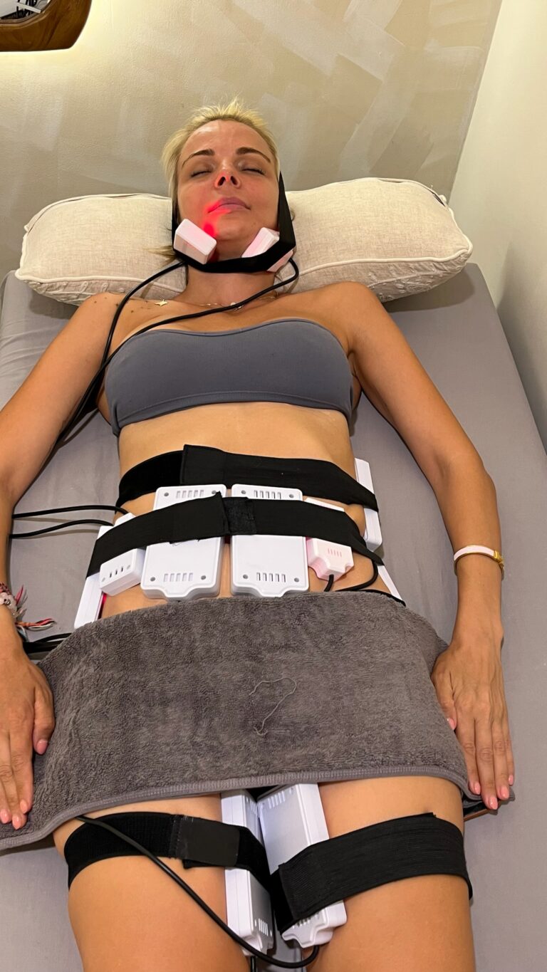 A client receives cold lipo laser treatment with pads secured around the chin, abdomen, and thighs.