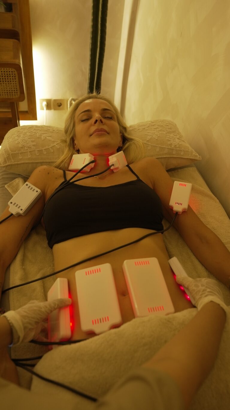 A client receives a cold lipo laser treatment with red-lit pads placed on the abdomen, arms, and neck.