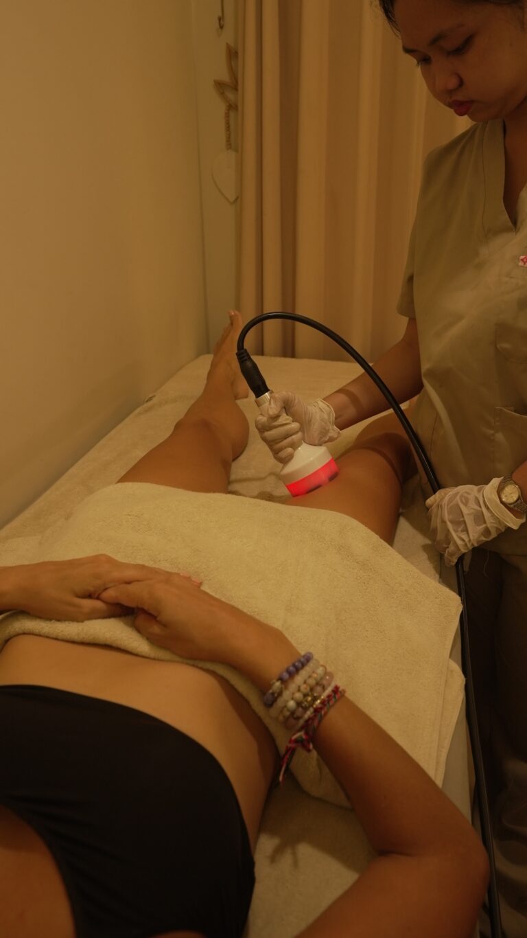 A therapist applies a handheld cavitation probe to a client’s thigh.