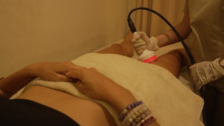A therapist applies a handheld treatment probe to a client's thigh.