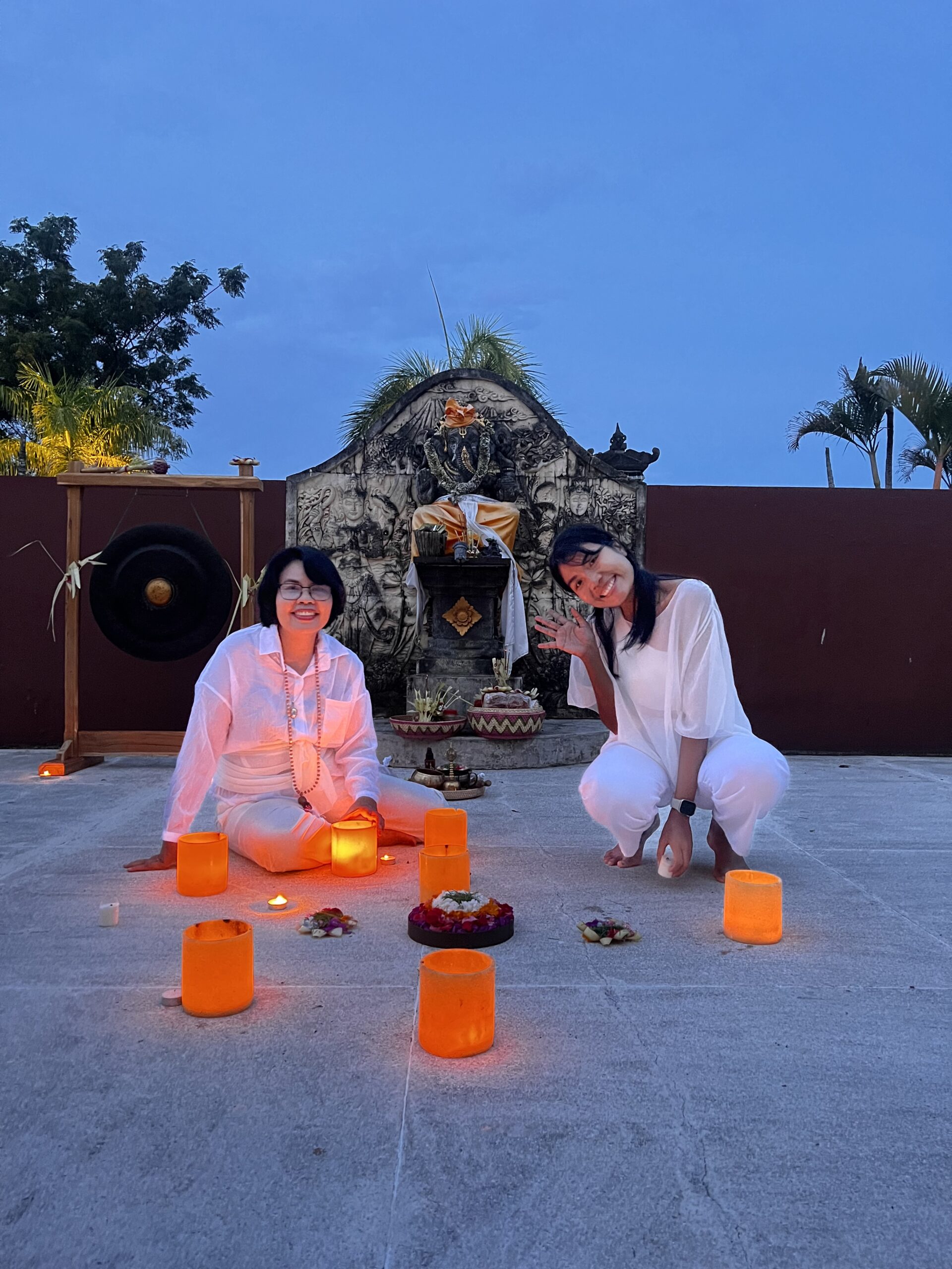 Candles and offerings before a stone shrine at dusk during an evening ceremony
